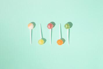Colorful lollipops arranged on a green background. Minimal candy flat lay concept