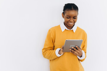 Happy black student girl in a yellow jacket holds a tablet and shows cheers on a white background