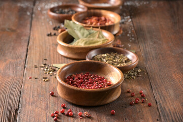 Various spices in a row of wooden bowls on rustic dark planks, copy space, selected focus