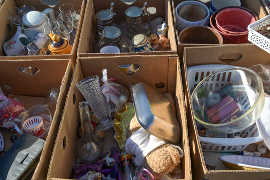Cardboard boxes with old used household items and tableware on a garage sale or flea market at a sunny weekend, selected focus