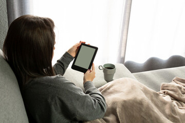 Young woman sitting on the sofa reading with her e-book.