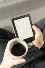 Relaxing moment of an unrecognizable boy reading an electronic book and holding a cup of coffee.