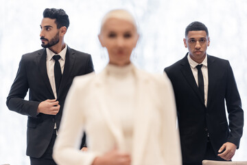 interracial bodyguards in formal wear escorting blurred businesswoman during business trip.