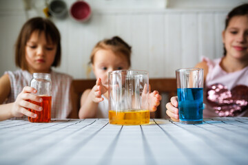 Three cute children play in the kitchen at home with colored liquids. Experiments with color at home.