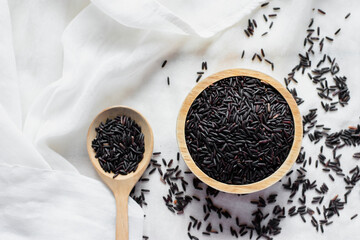 The black rice grains in a wooden cup rested on a white cloth surface, healthy food and diet concept.