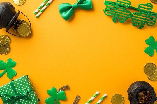 Top view photo of st patrick's day decor clover shaped party glasses straws green bow-tie giftbox horseshoe shamrocks pots with gold coins on isolated yellow background with blank space in the middle