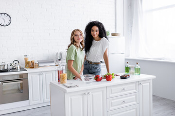 cheerful multiethnic lesbian couple standing together in modern kitchen.