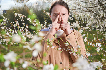 Woman allergic suffering from seasonal allergy at spring, posing in blossoming garden at...