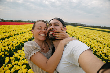 Caucasian couple taking a selfie in a flower field full of yellow and red tulips in the Netherlands