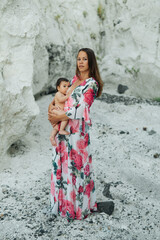 Caucasian Mother with a flower dress breastfeeding a one year old baby  on white rocks background