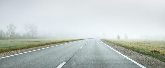 Panoramic view from the car of the empty highway through the fields and forest in a fog at sunrise....