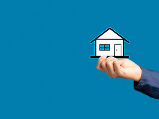 Fototapeta na wymiar Business and real estate concept. Close-up of hand holding a mini paper house while standing on a blue background.