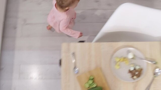 Little cute 2 years old girl having fun running around kitchen table instead of eating, Problems how to feed a child. Top view. 