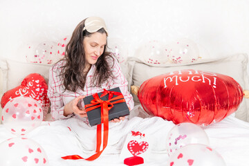 A beautiful woman in pink pajamas with a heart-shaped balloon lies on bed at home. Woman on Valentine's Day, birthday or anniversary. Love symbol