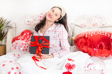A beautiful woman in pink pajamas with a heart-shaped balloon lies on bed at home. Woman on Valentine's Day, birthday or anniversary. Love symbol