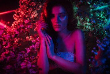 A fantastic shot of a girl in flowers with neon multicolored light and phantasmagoria. The concept...