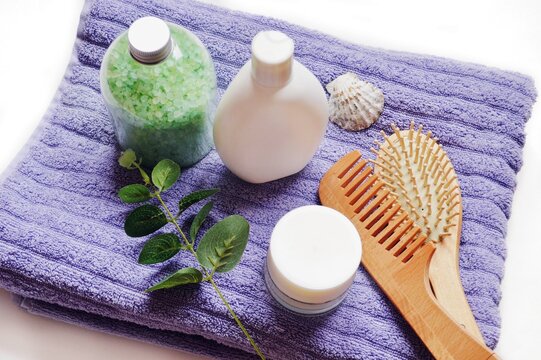 Flat lay composition beauty lifestyle photography. Green sea salt, white shampoo bottle, face cream, wooden brushes and eucalyptus leaves on a purple towel background. Natural organic cosmetics