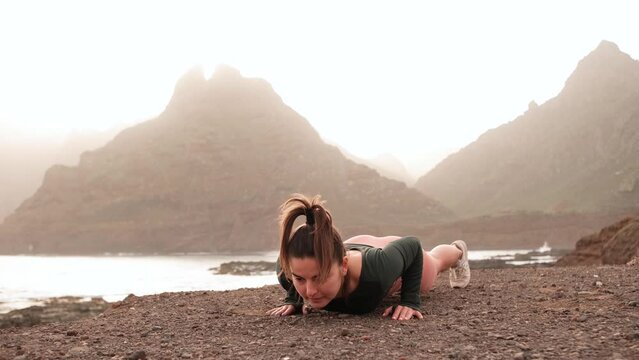 Young woman doing fitness exercises at sunrise or sunset on the beautiful island with mountains and ocean