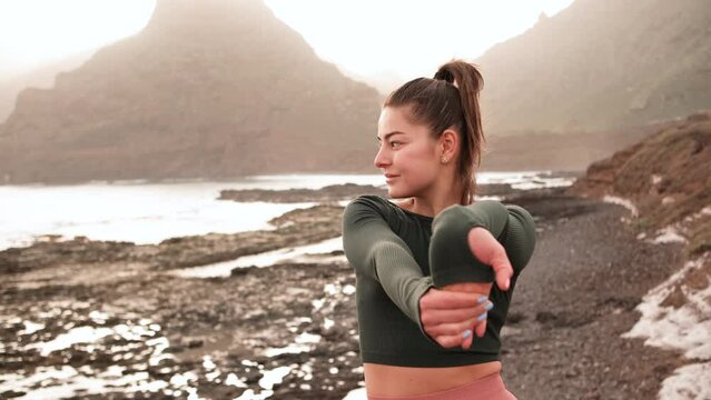 Young woman doing fitness exercises at sunrise or sunset on the beautiful island with mountains and ocean