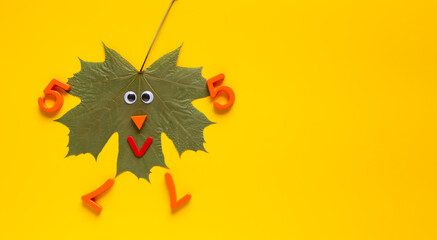 Yellow background with dry marple leaf with funny face, geometric shapes and numbers.
