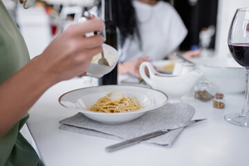 cropped view of woman holding bowl with grated cheese near pasta on plate.