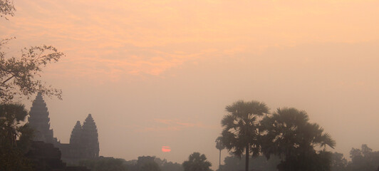 A pale orange sunrise in the blue sky over the Angkor Wat jungle.