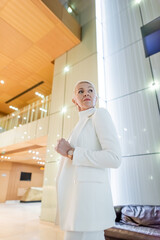 low angle view of wealthy businesswoman in white blazer looking away in modern hotel.