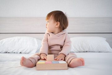 Happy preschool child girl sitting on the bed plays an educational game with blocks. Eco-friendly toys for children without plastic. Banner.