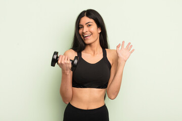young pretty hispanic woman smiling happily, waving hand, welcoming and greeting you. fitness...