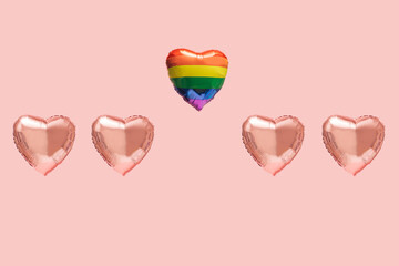 Four pink heart shaped balloons in line with rainbow color heart shaped balloon flying off above them. Pink background. LGBT liberation abstract concept.