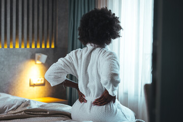 Young black woman sit on bed touching sore back feel morning backpain, upset african girl suffer...