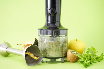 Black electrical hand blender and accessories with fruit on a green background, close up.