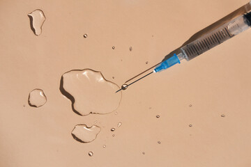 Drops of a transparent liquid and a sterile medical syringe on a beige background. Flat lay, place...