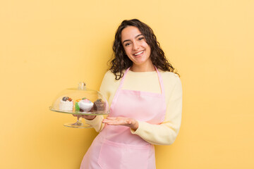 young pretty hispanic woman smiling cheerfully, feeling happy and showing a concept. chef and cakes concept - obrazy, fototapety, plakaty