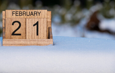 Wooden calendar of February 21 date standing in the snow in nature.