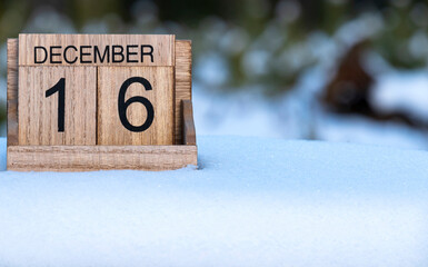 Wooden calendar of December 16 date standing in the snow in nature.