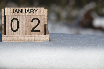 Wooden calendar of January 2 date standing in the snow in nature.