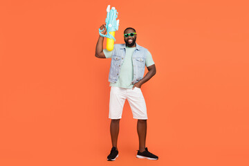 Photo of cool funky afro guy wear denim vest dark eyewear playing water gun isolated orange color background
