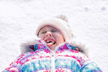 little funny girl without front milk teeth, lies on the snow and grimaces