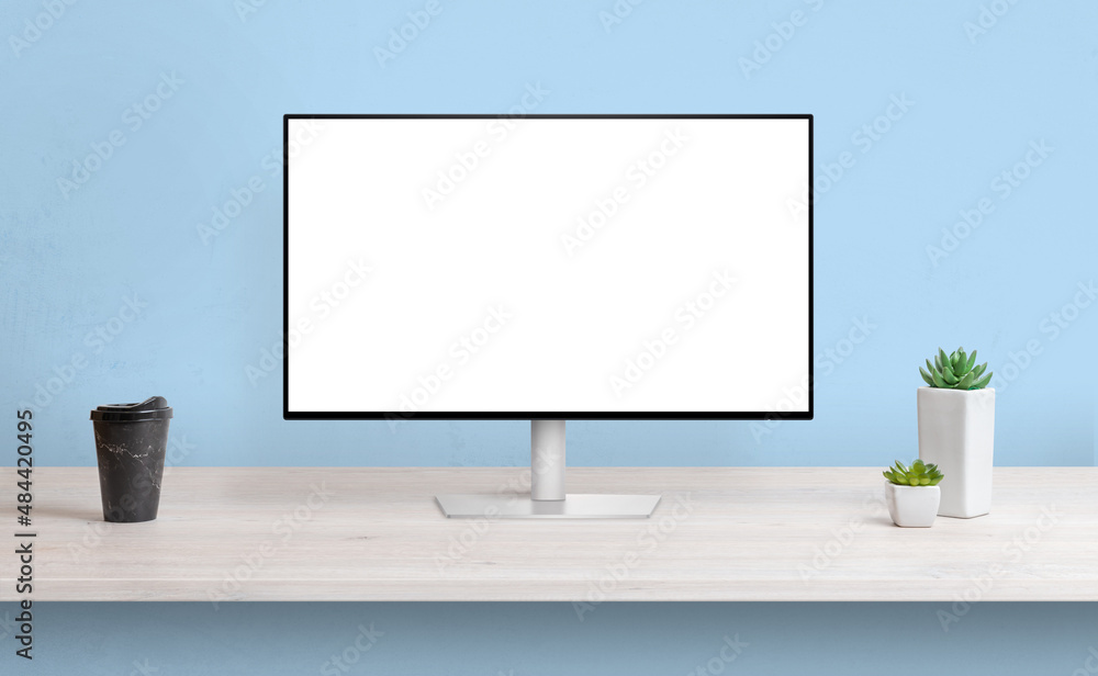Aufkleber Computer display on work desk with isolated screen for web page presentation. Coffee and plants beside. Blue wall in background