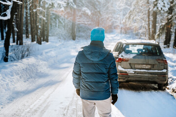 A young man stands near a car in a snowy forest in winter on a sunny day