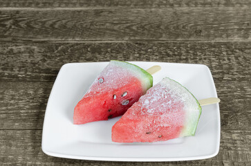 Frozen watermelon fruit desserts on a stick, in a plate on an old wooden background. Selective focus