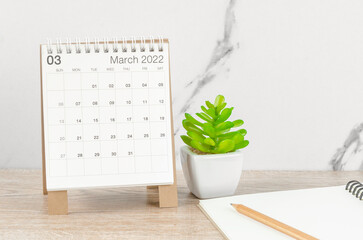 March 2022 desk calendar with plant on wooden table.