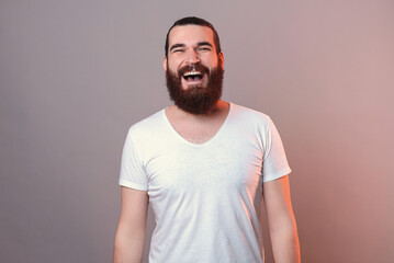 Friendly bearded man is smiling at the camera. Studio portrait over grey background.