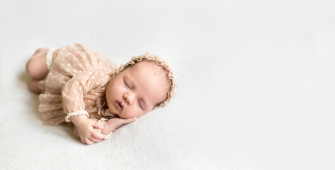 A cute newborn baby sleeps sweetly with his palms pressed to his cheek and his mouth slightly open. A girl in a lace cap and a bodysuit. Care, care and love from birth