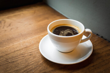 A cup of black coffee on the wooden windowsill, natural light