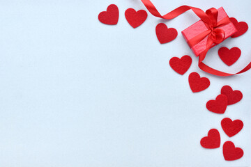 Valentines Day background. Red gift box with ribbon and felt hearts on a pastel blue background....