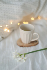 Fototapeta na wymiar Cup of lemon tea, daffodil flower and accessorries on bed. Breakfast in bed. Morning. Spring. 