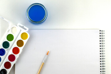 watercolor paints brush jar with water and sketchbook on a white background