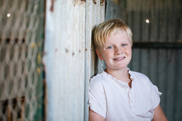 Cute blonde pre-teen boy with relaxed pose in rustic outdoor setting